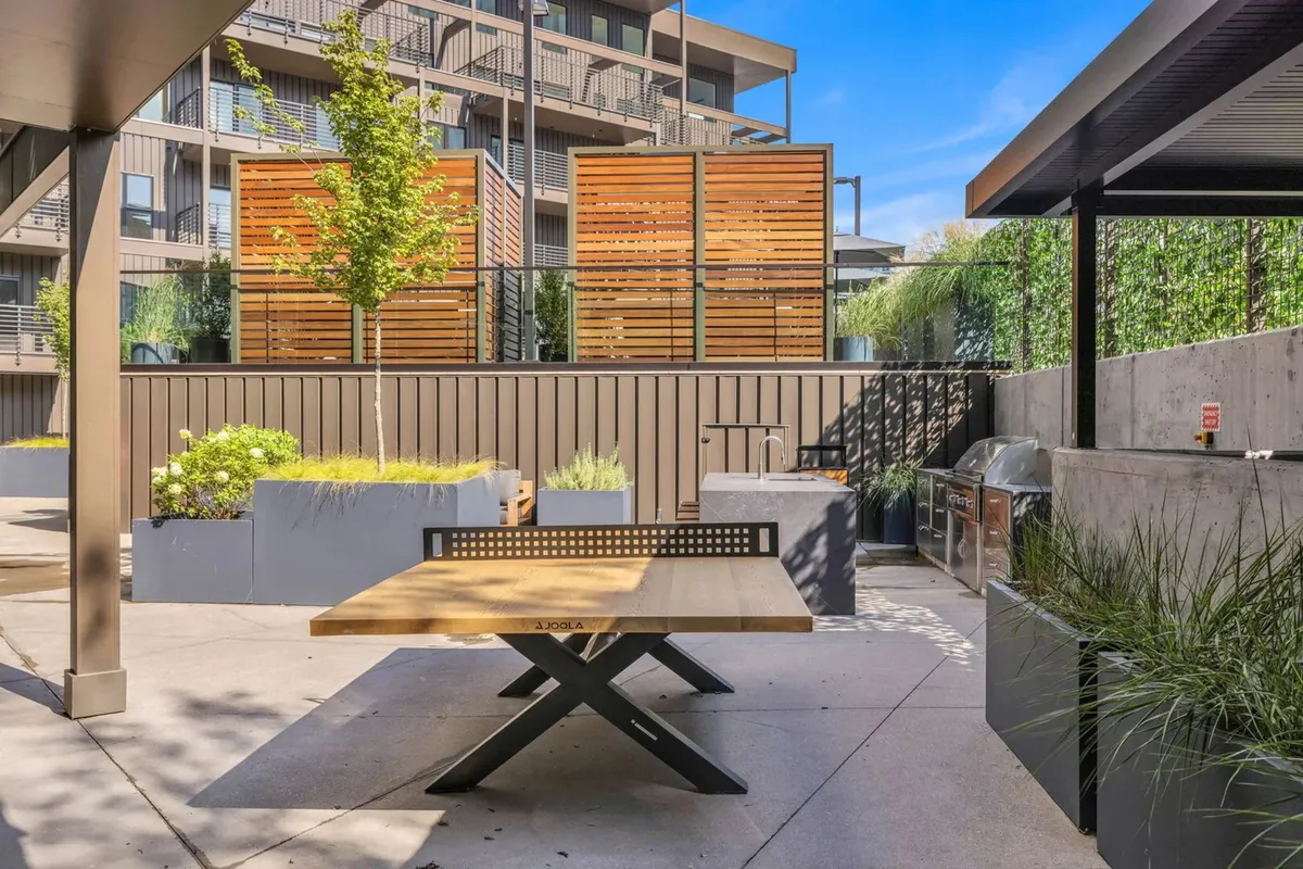 The image spotlights an outdoor communal space with a dining table, wooden privacy screens, and a grilling area. The setup encourages group barbecues and al fresco dining, enhanced by a relaxed and communal ambiance.