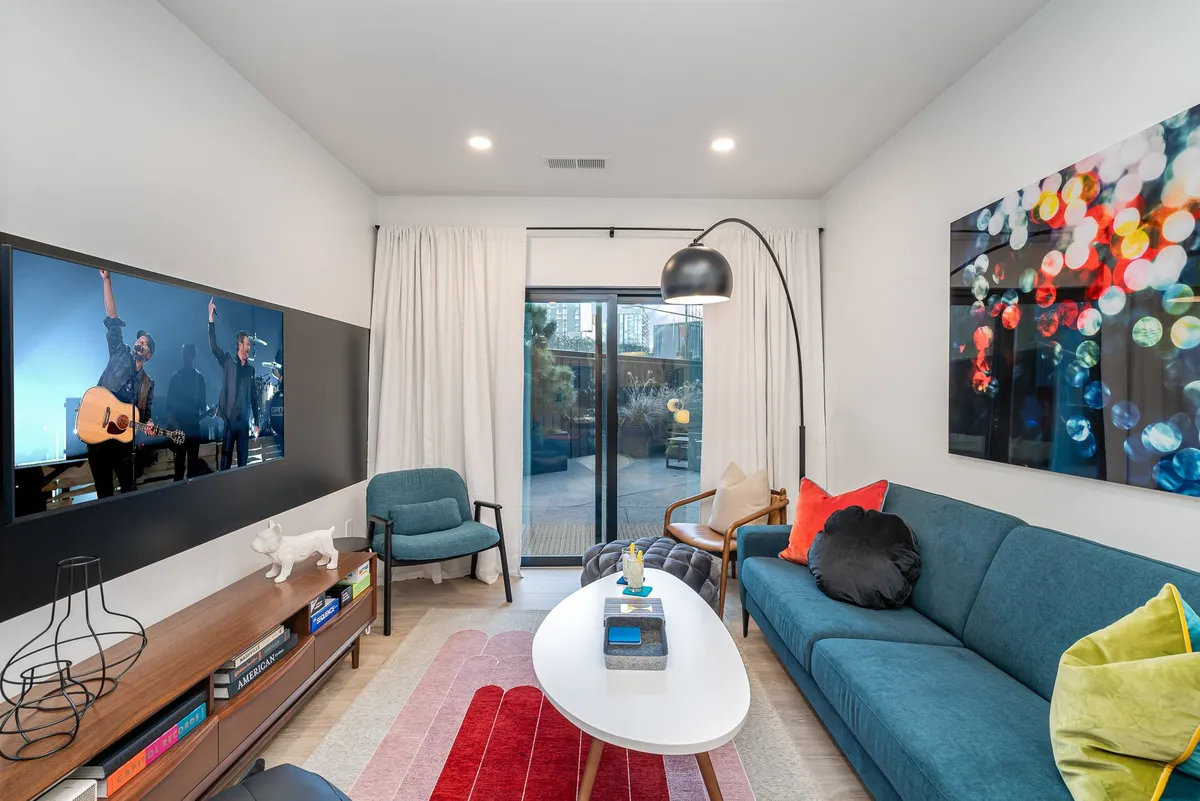 A spacious living area featuring a cozy sofa with colorful cushions, a large television screen, modern coffee table, and wall-mounted artwork. The layout is ideal for group gatherings, movie nights, or relaxing with friends, and it reflects a comfortable, contemporary ambiance.