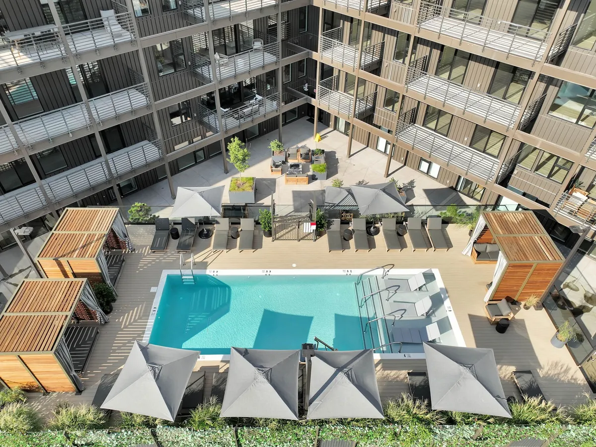 An inviting view of the patio and pool area just outside, featuring lounge chairs, umbrellas, and lush landscaping. The outdoor seating flows seamlessly from the indoor living spaces, emphasizing the easy access and connection between indoor relaxation and outdoor fun.