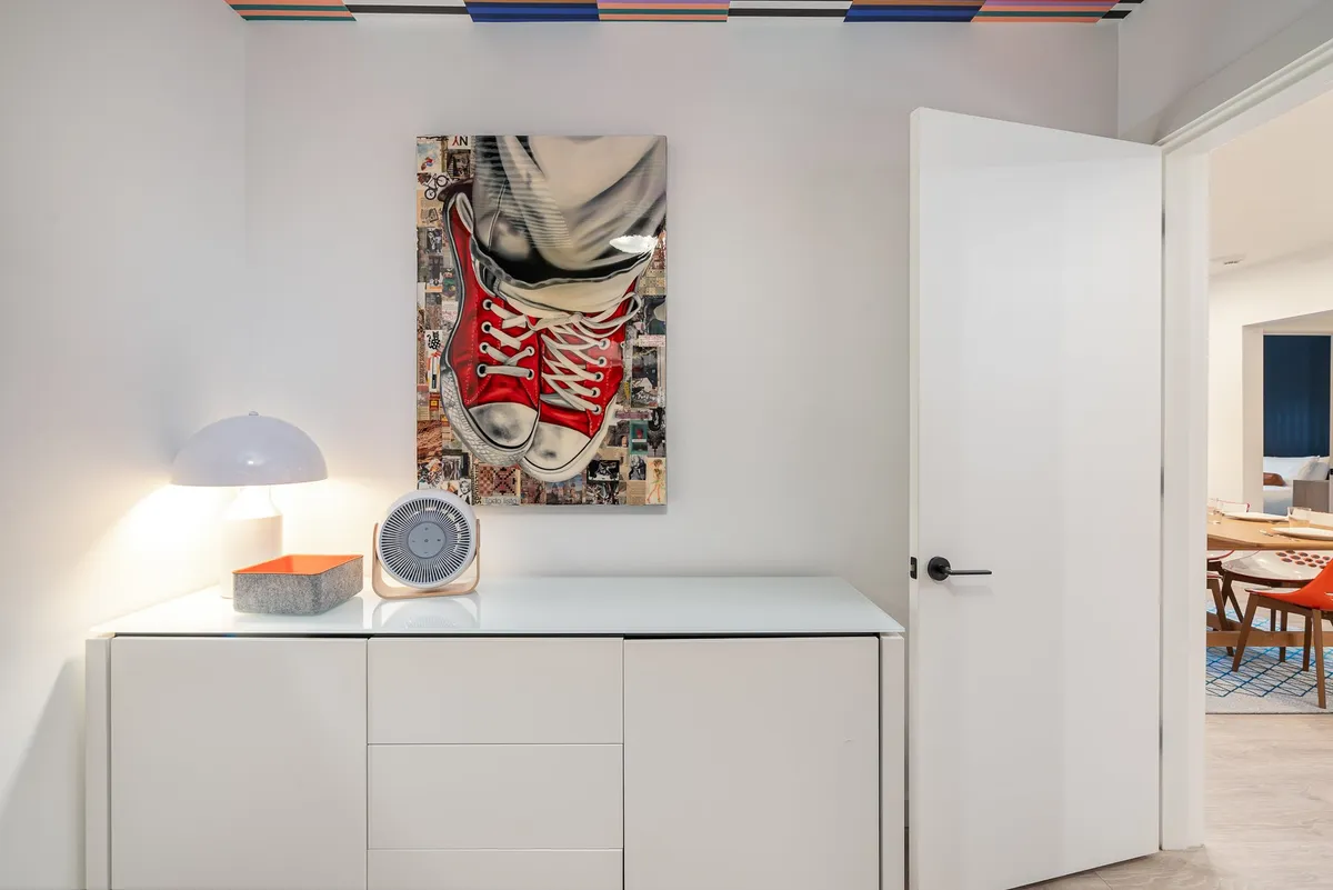 A stylish entryway featuring a large artwork of a sneaker, a minimalist storage unit, a decorative clock, and modern lighting. The setting feels welcoming and organized, suggesting the first impression as you enter the building.