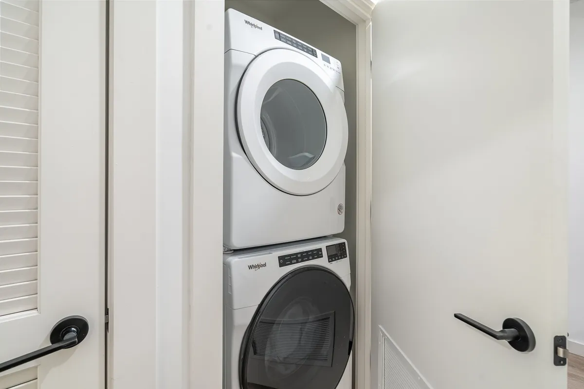 A practical in-unit laundry area featuring stacked washer and dryer, modern appliances, and a clear, accessible door handle. The space is clean and emphasizes convenience.