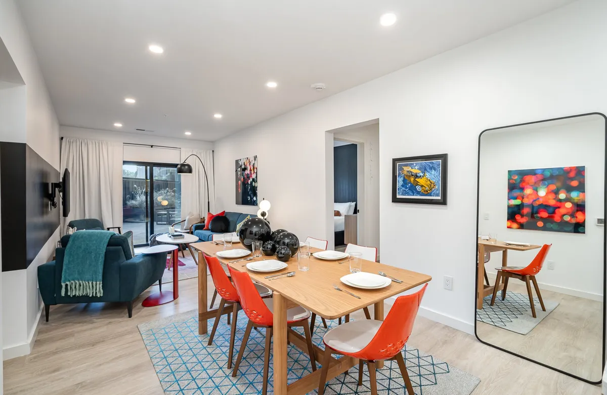 A vibrant dining area with a table surrounded by red chairs, a green sofa, eye-catching artwork, and a large mirror that enhances the open, airy feel. The setting is lively yet comfortable, ideal for group meals or game nights.